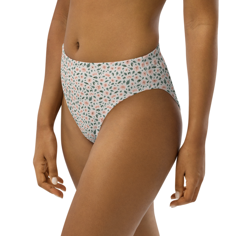 Woman wearing high-waisted bikini bottom with floral pattern in pink and green on white background.