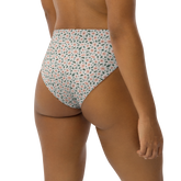 Woman wearing high-waisted bikini bottom with floral pattern of pink flowers and green leaves on white background.
